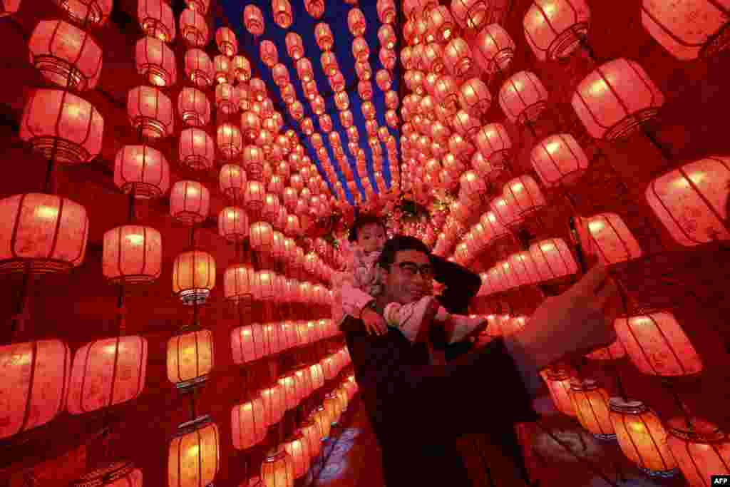 Seorang pria sambil menggendong putrinya, mengambil foto di samping lampion-lampion yang dihiasi lampu selama Festival Lampion, yang menandai berakhirnya perayaan Tahun Baru Imlek di Taiyuan, provinsi Shanxi, China utara. (Foto: STR / AFP)&nbsp;