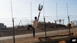 A protester holds a Palestinian flag in front of Israeli soldiers during a protest against the controversial Israeli barrier in the West Bank village of Bilin, near Ramallah, 26 Nov 2010