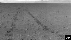 Crno-bela fotografija tragova točkova marsovskog rovera Kjuriositi u pesku crvene planete