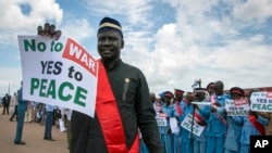 FILE - South Sudanese people hold signs as they await the arrival back in the country of South Sudan's President Salva Kiir, at the airport in Juba, South Sudan, June 22, 2018. 