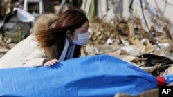 Tayo Kitamura, 40, kneels in the street to caress and talk to the wrapped body of her mother Kuniko Kitamura, 69, after Japanese firemen discovered the dead woman inside the ruins of her home in Onagawa, March 19, 2011