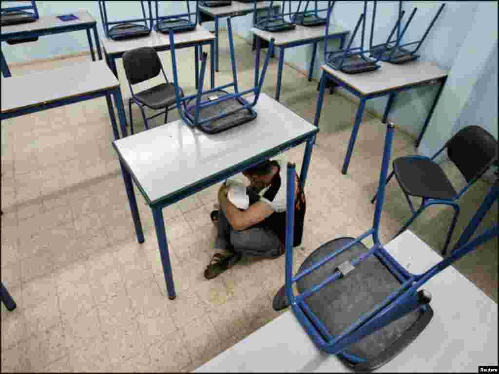 اسرائیل میں راکٹ حملوں کے دوران ایک طالبعلم اسکول میں میز کے نیچے چھپ کر دعاوں کی کتاب پڑھ رہاہے