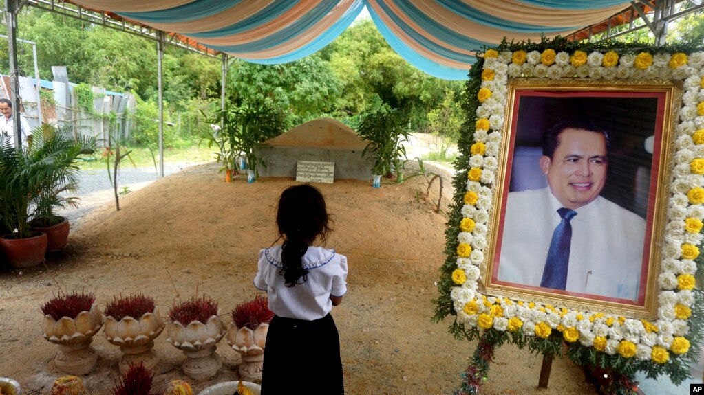 In this Nov. 20, 2016 photo, a girl stands by a portrait of Kem Ley, a Cambodian prominent political analyst, at his grave in Ang Takok, Cambodia. (AP Photo/Denis Gray)