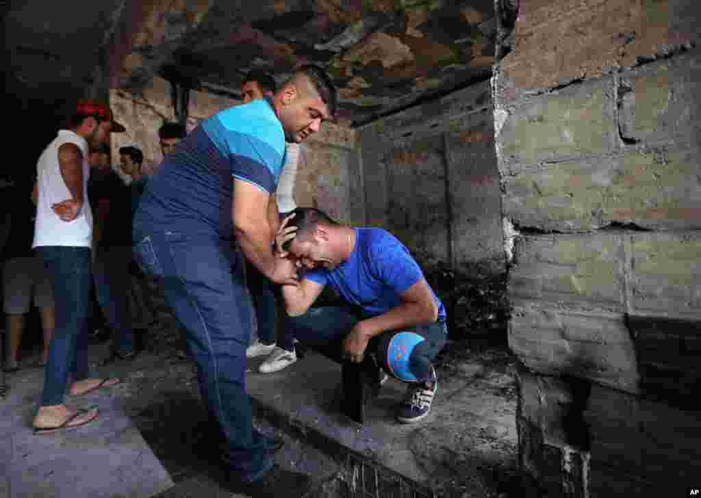 Iraqi men grieve at the scene of a deadly suicide car bomb at a commercial area in Karrada, Baghdad, July 4, 2016.