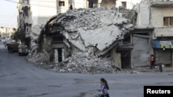 A girl runs past damaged buildings in the rebel-controlled area of Maaret al-Numan town in Idlib province, Syria, Dec. 21, 2015.