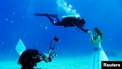 A model opens her mouth to breathe from a scuba tank as Israeli photographer Johannes Felten (L) takes pictures during an underwater photo shoot in the Red Sea in the resort city of Eilat, Oct. 22, 2013.