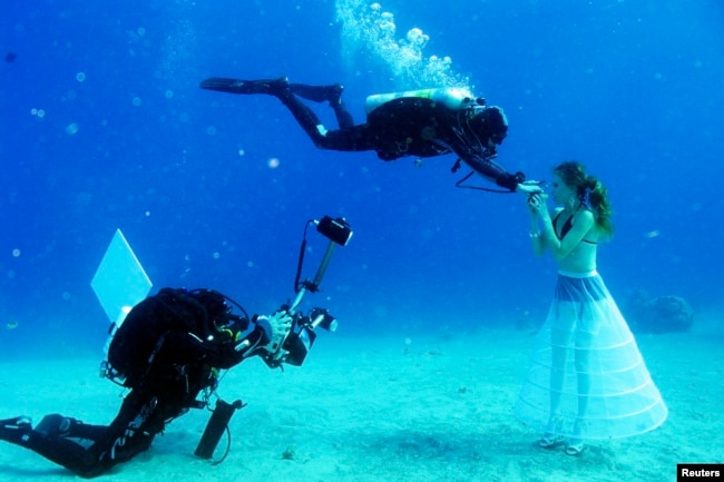 A model opens her mouth to breathe from a scuba tank as Israeli photographer Johannes Felten (L) takes pictures during an underwater photo shoot in the Red Sea in the resort city of Eilat, Oct. 22, 2013.