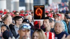 A man in the crowd holds a QAnon sign with the group's abbreviation of their rallying cry 