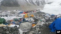 FILE – In this April 28, 2015 file photo, guides and climbers stand beside gear piled up after an avalanche triggered by the massive 7.8 magnitude earthquake hit the area.