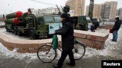 A man walks with his bicycle next to air defense system displays in front of the Russian Army Theater in Moscow, Dec. 8, 2014.