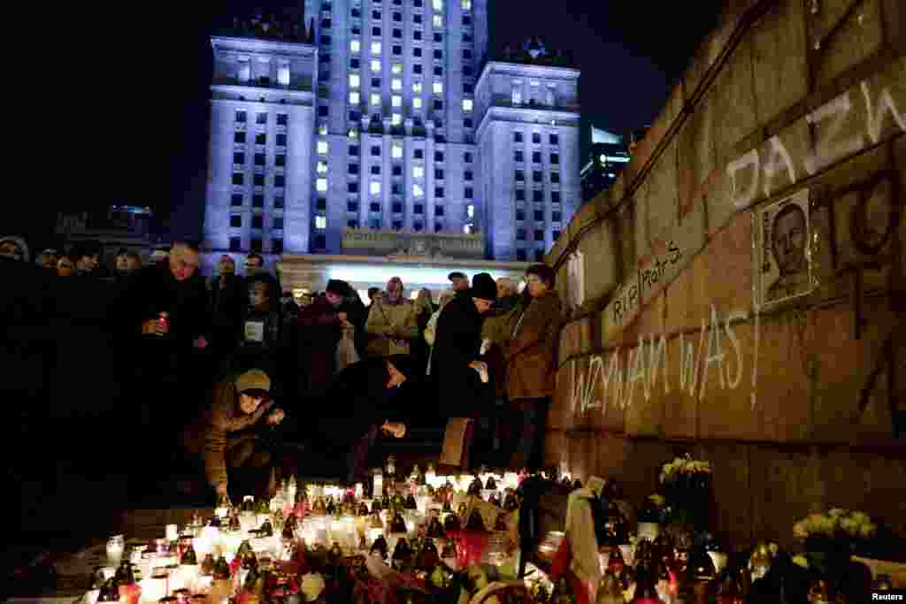 People gather and lay candles in the place where a man set himself on fire in anti-government protest in front of the Palace of Culture and Science in Warsaw, Poland, Nov. 6, 2017.