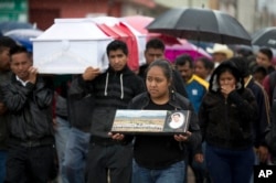 FILE - A young woman walks with a photo of Jesus Cadena in his funeral procession in Nochixtlan, Oaxaca state, Mexico, June 21, 2016. It was two days after he was killed in a clash between police and striking teachers.