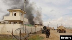 Một thành viên lực lượng an ninh Afghan đi qua một tòa nhà bốc khói nghi ngút sau một cuộc tấn công của Taliban vào khu vực quận Gereshk, tỉnh Helmand, Afghanistan, ngày 9 tháng 3 năm 2016. 