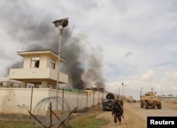 A member of the Afghan security forces walks as smoke billows from a building after a Taliban attack in Gereshk district of Helmand province, Afghanistan, March 9, 2016.