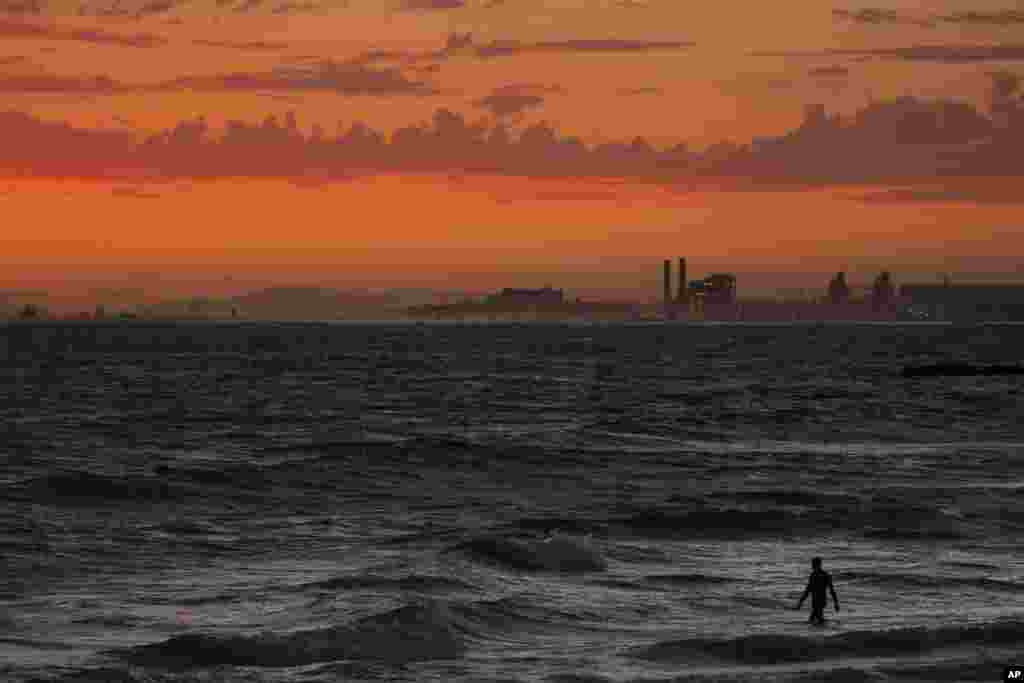 A man wades into the ocean at sunset, June 22, 2021, in Newport Beach, California.