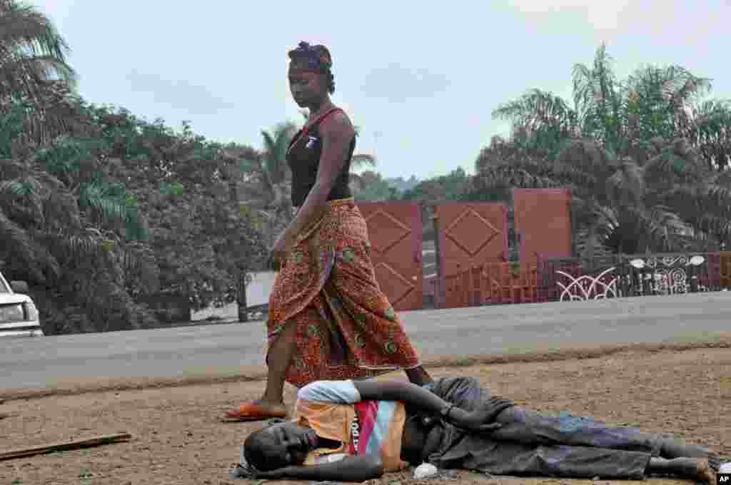 A woman looks down as she walks past a man suspected of suffering from the Ebola virus in a busy part of Monrovia, Liberia, Sept. 12, 2014.