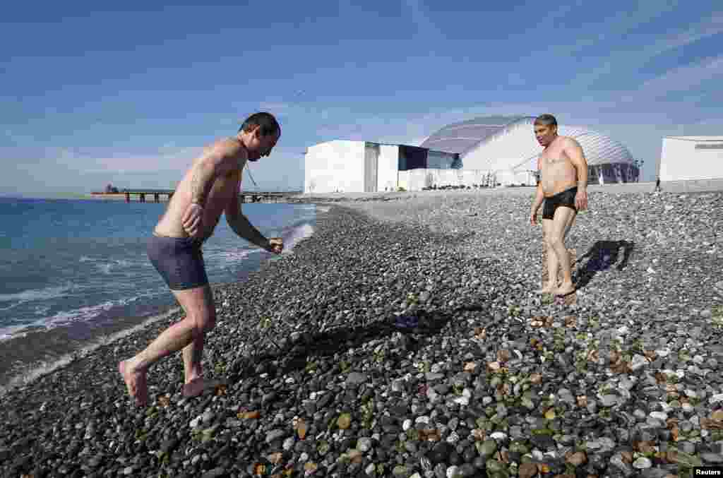 Seorang pria keluar dari Laut Hitam di Sochi, sementara kompleks Olympic Park tempat berlangsungnya Olimpiade terlihat di latar belakang.
