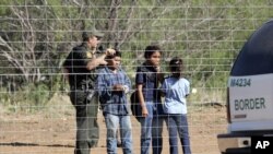 FILE - A Border Patrol agent stands on a ranch fence line with children taken into custody, in South Texas brush country north of Laredo, Texas.
