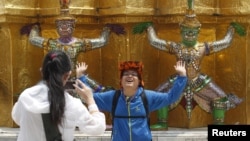 FILE - A Chinese tourist strikes a similar pose to statues as they visit the Grand Palace in Bangkok, March 23, 2015. 