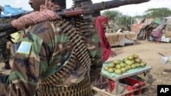 FILE - A fruit seller looks across as a Somali government soldier stands guard in Afgoye, west of the capital Mogadishu, in Somalia.