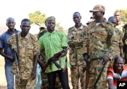 FILE - In this photo taken Jan. 6, 2019, government and opposition soldiers pose for a picture in the government barracks in Kajo Keji town, where 10 opposition soldiers were staying with the government troops in a makeshift soldier swap, in Kajo Keji county, South Sudan. Since a fragile peace deal was signed in September 2018, South Sudan's previously warring parties have been working to rebuild trust in some of the areas hardest hit by the war.