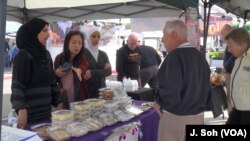 Noor al Mousa sells Syrian sweets as Tan Jakwani and an interpreter help at a farmers market in Phoenix, Arizona.