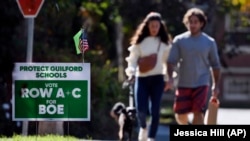 People walk near one of many signs around town centered around the upcoming Nov. 2 election, seen on Tuesday, Oct. 19, 2021. The school system is seeing opposition to the efforts made to gain equity and inclusion in schools in Guilford, Conn. (AP Photo/Jessica Hill)