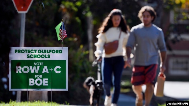 People walk near one of many signs around town centered around the upcoming Nov. 2 election, seen on Tuesday, Oct. 19, 2021. The school system is seeing opposition to the efforts made to gain equity and inclusion in schools in Guilford, Conn. (AP Photo/Jessica Hill)