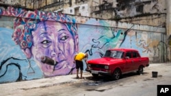 FILE - A man washes a car next to a mural in Havana, Cuba, Aug. 9, 2018. The country is softening a new law that would have created a corps of art inspectors able to shut down displays or performances deemed objectionable.