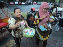 Penyandang difabel (kiri) memberikan souvenir buatannya pada warga yang melintas dalam perayaan Hari Disabilitas Dunia, di Solo, Senin sore, 3 Desember 2018. (Foto: VOA/Yudha)