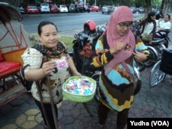 Penyandang difabel (kiri) memberikan souvenir buatannya pada warga yang melintas dalam perayaan Hari Disabilitas Dunia, di Solo, Senin sore, 3 Desember 2018. (Foto: VOA/Yudha)