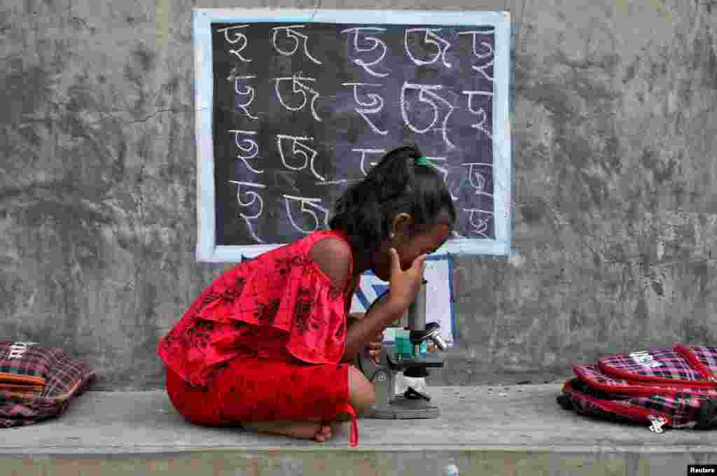 A girl who does not have access to internet and other equipment uses a microscope as she attends an open-air class outside a house with its walls turned into blackboards, following the closure of school due to the COVID-19&nbsp;outbreak, at Joba Attpara village in Paschim Bardhaman district in the eastern state of West Bengal, India,&nbsp;