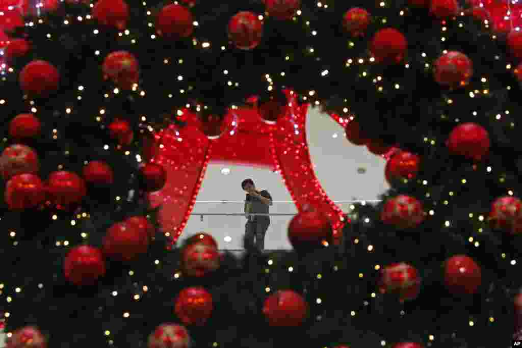 A shopper is seen through Christmas decorations as he uses his smartphone to take a photo at a mall in Kuala Lumpur, Malaysia.