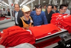 FILE - Prime Minister Hun Sen, center, leans over a garment worker during a visit to a factory outside Phnom Penh, Cambodia, Aug. 30, 2017.
