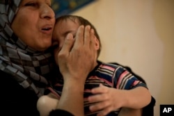 FILE - A worker comforts a toddler at Salhiya Orphanage, which now hosts foreign and Iraqi children of Islamic State militants, in Baghdad, Iraq, Aug. 16, 2018. The war to drive out IS militants left tens of thousands of orphans.