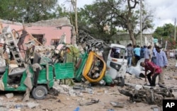 Somalis walk near destroyed vehicles at the scene of a car bomb blast and gun battle targeting a restaurant in Mogadishu, June 15, 2017.