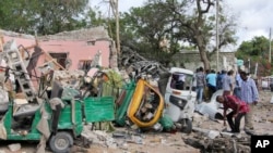 Warga Somalia berjalan di dekat kendaraan yang hancur di lokasi ledakan bom mobil dan pertempuran senjata yang menarget sebuah restoran di Mogadishu, 15 Juni 2017. (AP Photo/Farah Abdi Warsameh).
