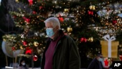 A man wearing a face mask to protect against coronavirus, walks in front of the Christmas tree at Syntagma square in Athens, Greece, Dec. 1, 2021.