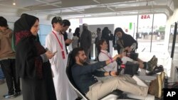Hostesses in black robes and headscarves give instructions to foreign visitors trying out a simulator at a Formula-E race on the outskirts of Riyadh, Saudi Arabia on Saturday, Dec. 15, 2018. 