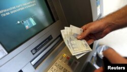 A man withdraws 60 Euros, the maximum amount allowed after the imposed capital controls in Greek banks, at a National Bank of Greece ATM in Piraeus port near Athens, Greece, June 30, 2015. 