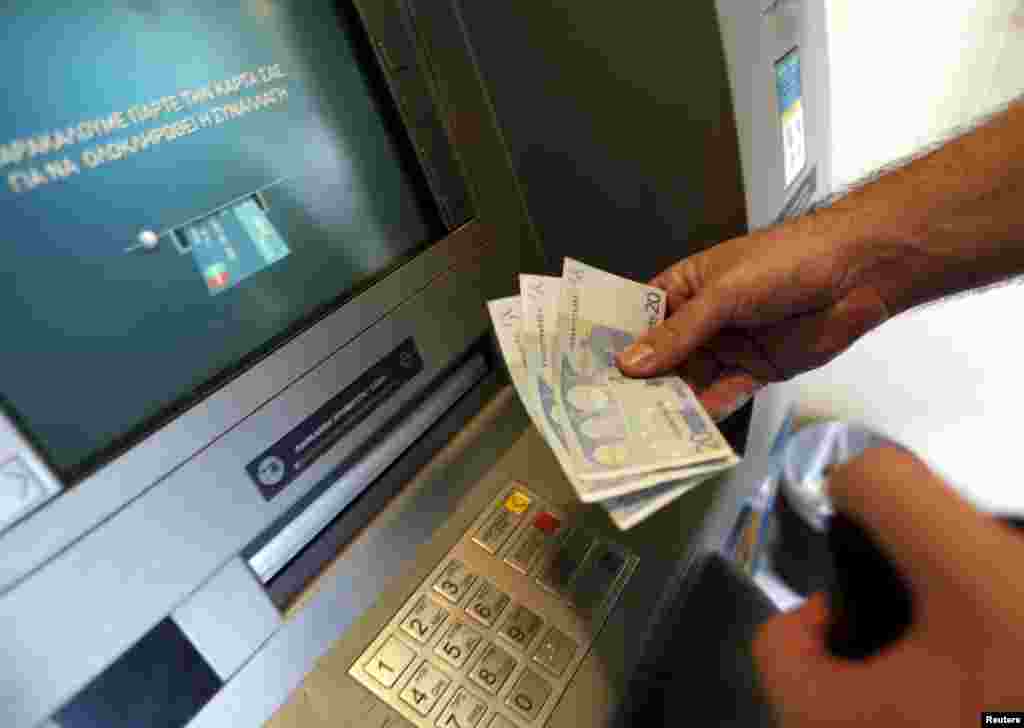 Seorang pria menarik uang 60 euro, batas maksimum yang diperbolehkan menyusul kontrol modal di bank-bank Yunani, di ATM National Bank of Greece di pelabuhan Piraeus dekat Athena (30/6).&nbsp;​(Reuters/Yannis Behrakis)