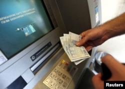 A man withdraws sixty Euros, the maximum amount allowed after the imposed capital controls in Greek banks, at a National Bank of Greece ATM in Piraeus port near Athens, Greece, June 30, 2015.