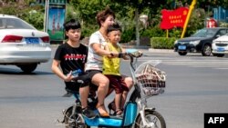 Seorang perempuan naik skuter dengan dua anaknya di Huaxian, provinsi Henan, China. China tengah berupaya mengatasi masalah penduduknya yang menua dengan memperlonggar aturan pembatasan jumlah anak.