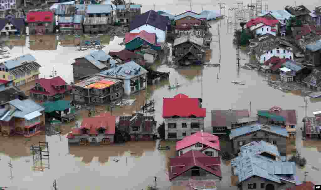 Flood-affected people row boats past partially submerged buildings in floodwaters in Srinagar, India,