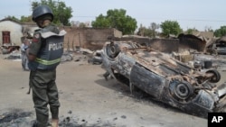 FILE - A Nigerian policeman stands guard by burned out cars and houses, following an attack by suspected Islamic extremists in Kawuri, Maiduguri, Nigeria.