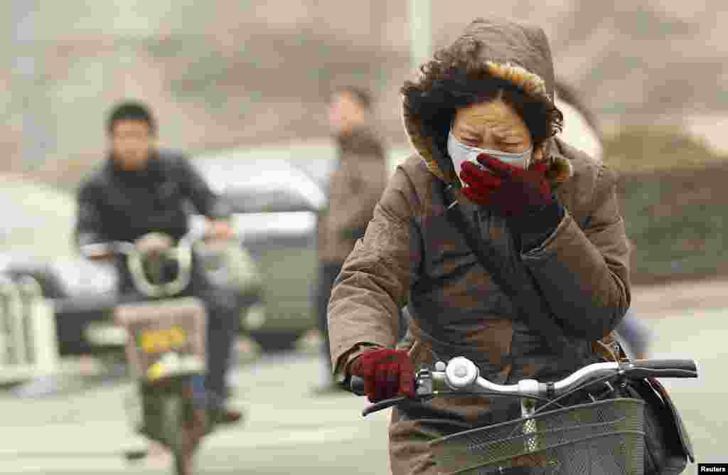 A woman wearing a mask rides her bicycle along a street on a hazy morning in Beijing, China.