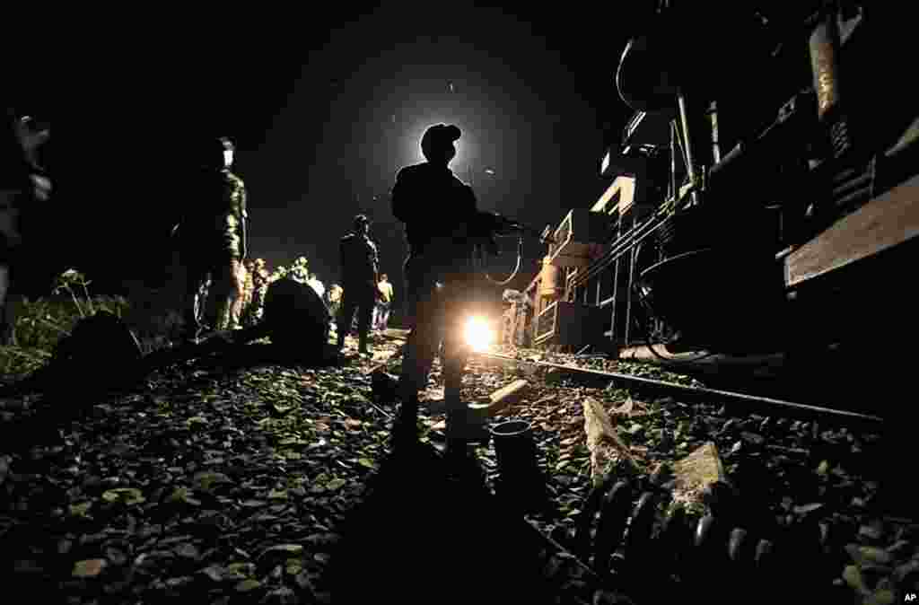 July 11: An Indian security force officer stands next to a derailed passenger train, near Bhatkuchi, India. Fifty passengers were injured as four coaches of the Guwahati-Puri Express derailed following a possible explosion. (AP Photo/Anupam Nath)