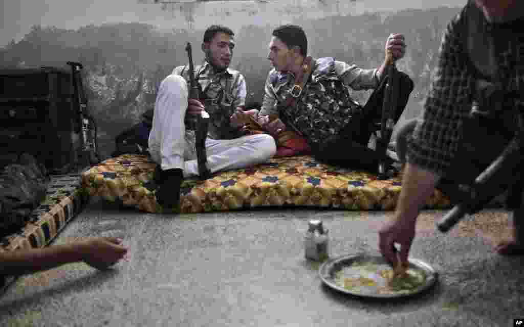 A Syrian rebel fighter, right, eats while others chat as they wait for transportation to go fight government forces in Aleppo, September 10, 2012. 