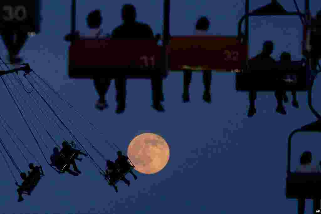 The moon rises as people sit on rides at the State Fair Meadowlands in East Rutherford, New Jersey, USA, July 1, 2015.