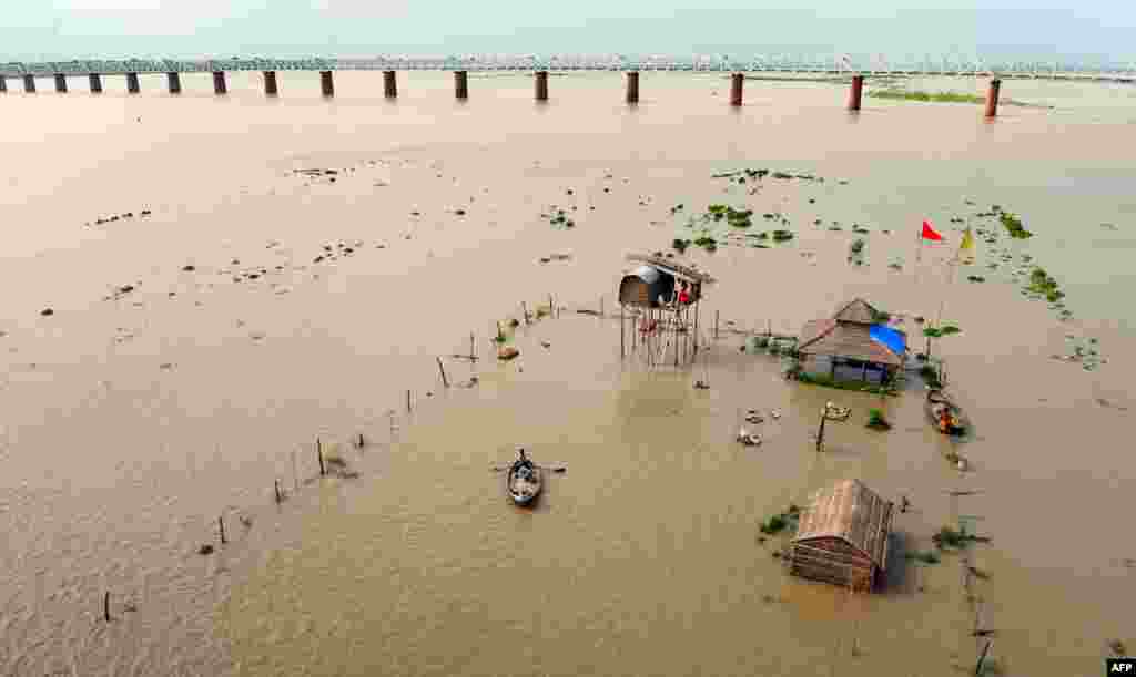 An Indian boatman rows passengers from submerged huts of &#39;sadhus&#39; - holy men - on the flooded banks of the Ganga river after water levels rose, in Allahabad. Heavy rain in several areas of north India has caused rivers to reach dangerous levels and flooding has occured in various places.